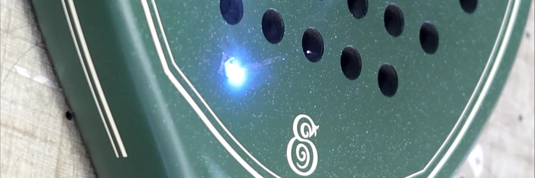 A laser engraving the face of a green Eterna padel racket, the beam lit blue against the matte frame