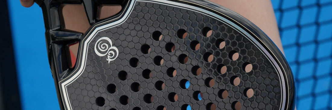 The solid, perforated face of an Eterna padel racket, held on a blue court beside the net