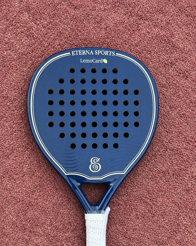 Soho Blue Glossy padel racket engraved with a brand name on the Crown, on a clay court