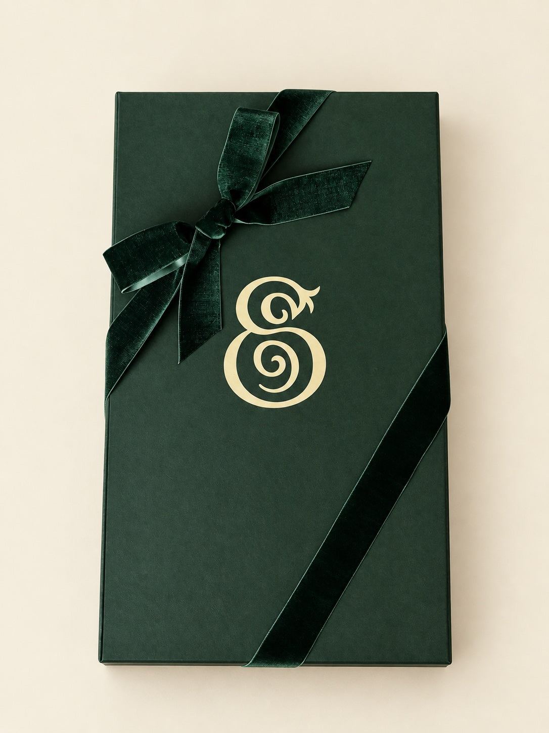 Closed dark green Eterna gift box with a cream monogram and velvet ribbon bow.